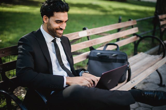pexels-ketut-subiyanto-4962589 a smiling businessman man using a laptop on a park bench